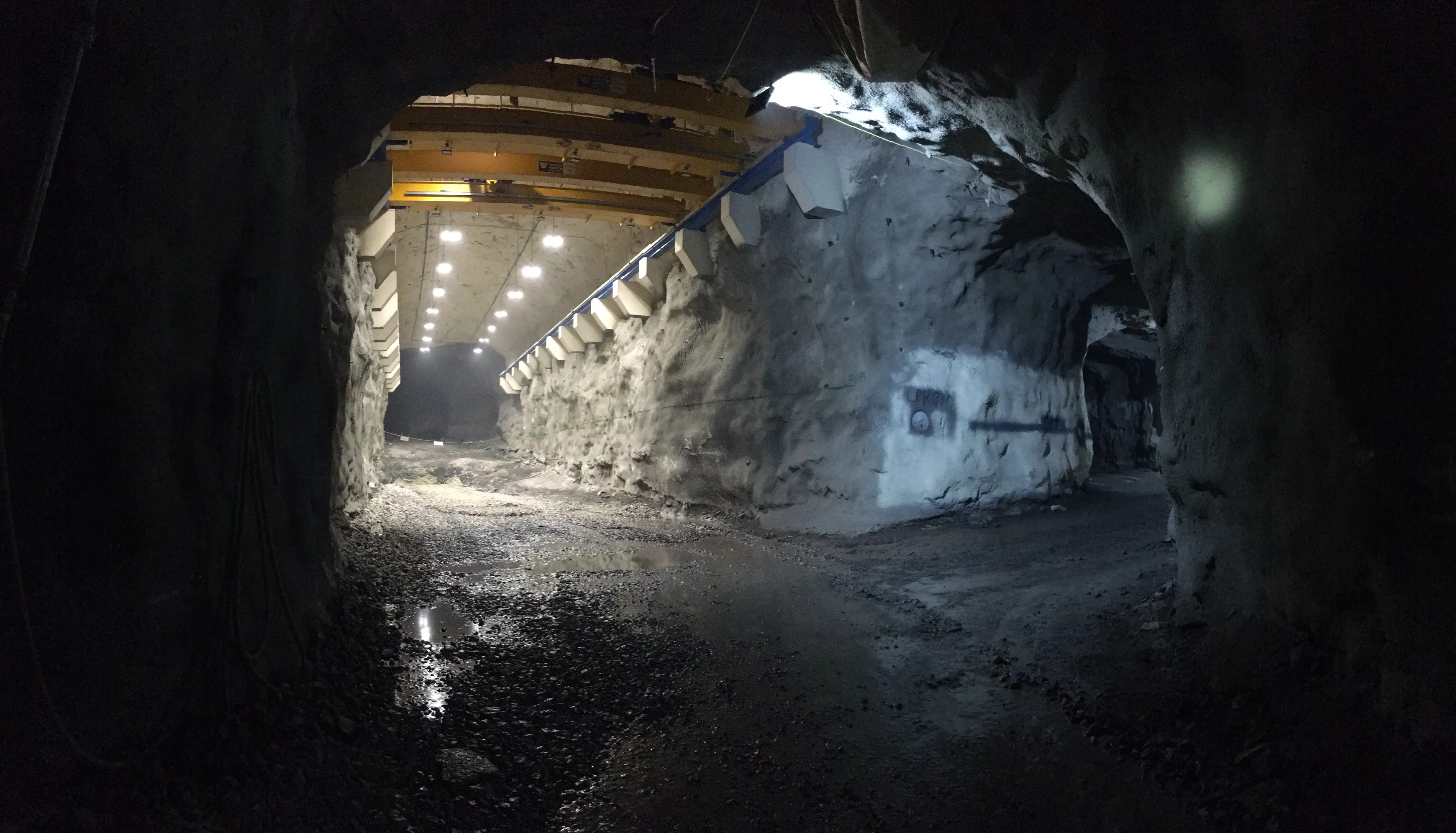 Underground mine workshop cavern with yellow overhead gantry crane and wet rock floor