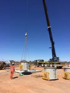 Mobile crane lowering surface vent fan equipment into place at a mine site with worker supervising
