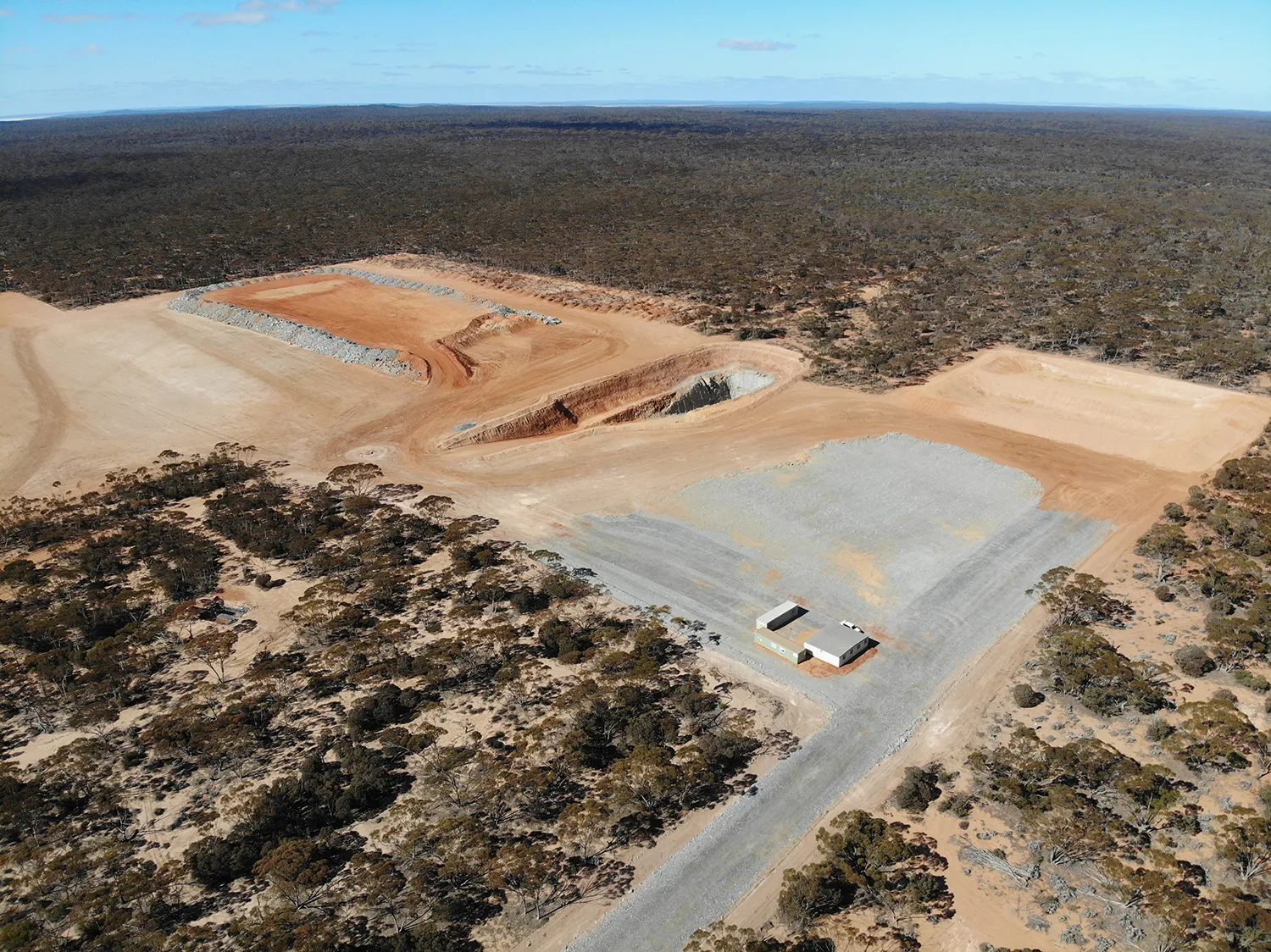 Aerial view of cleared mine site pad with small buildings surrounded by bushland scrub
