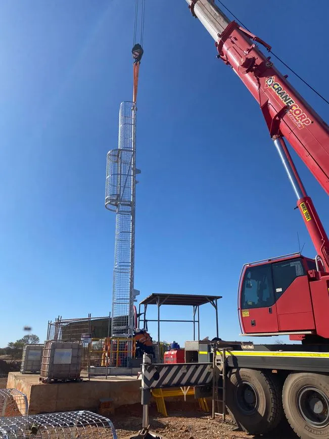 Mobile crane lifting a caged ladderway section into position at an underground dewatering site