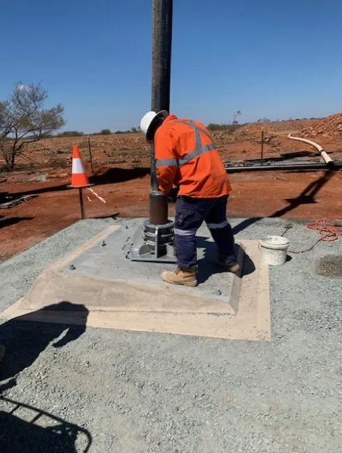 Worker in high-vis fitting a vertical pump column onto a concrete plinth at a remote site