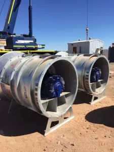 Two large galvanised axial ventilation fans with blue motors staged outdoors before installation