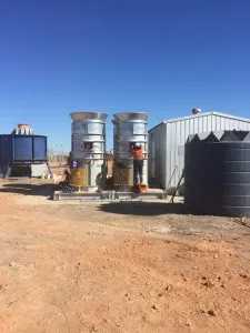 Twin surface vent fans on concrete plinths beside a water tank and shed at a mine site