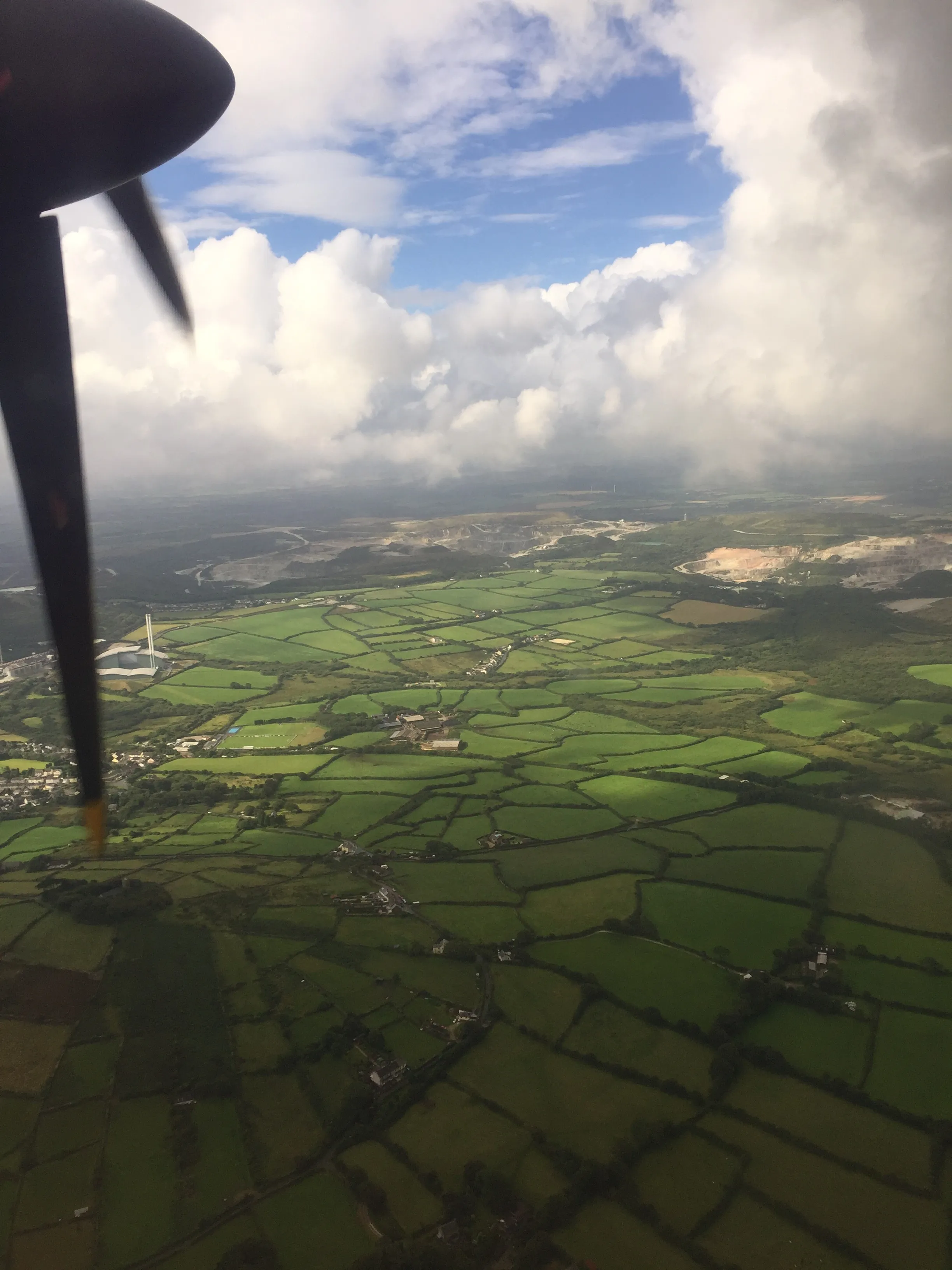 Aerial view from an aircraft propeller over patchwork fields and a distant quarry near Cornwall