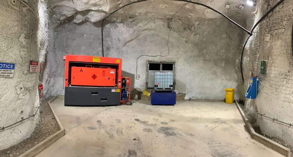 Underground mine fuel bay with orange diesel storage tank, IBC container and safety signage on rock-bolted walls