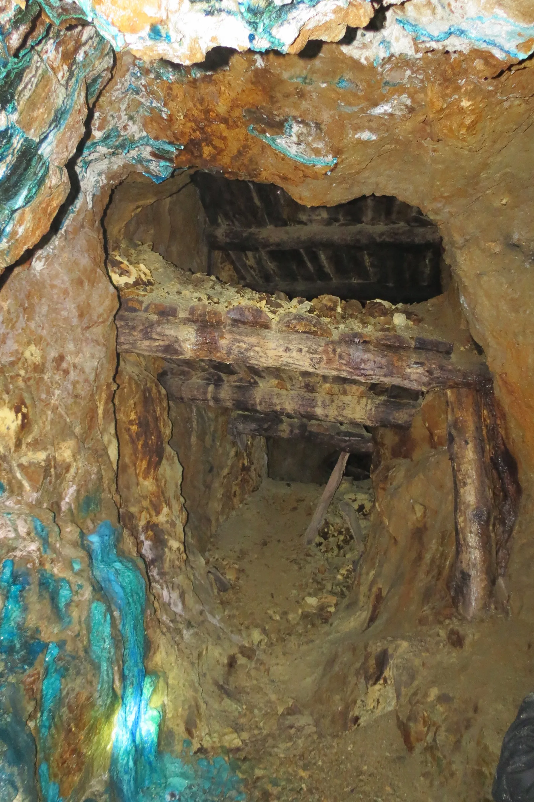 Old timber-supported mine tunnel with copper-stained blue and orange mineralised rock walls
