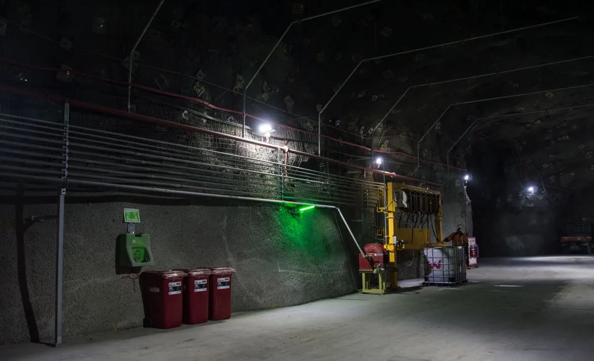 Underground mine service bay with mesh-lined walls, safety bins, eyewash station and yellow equipment rack