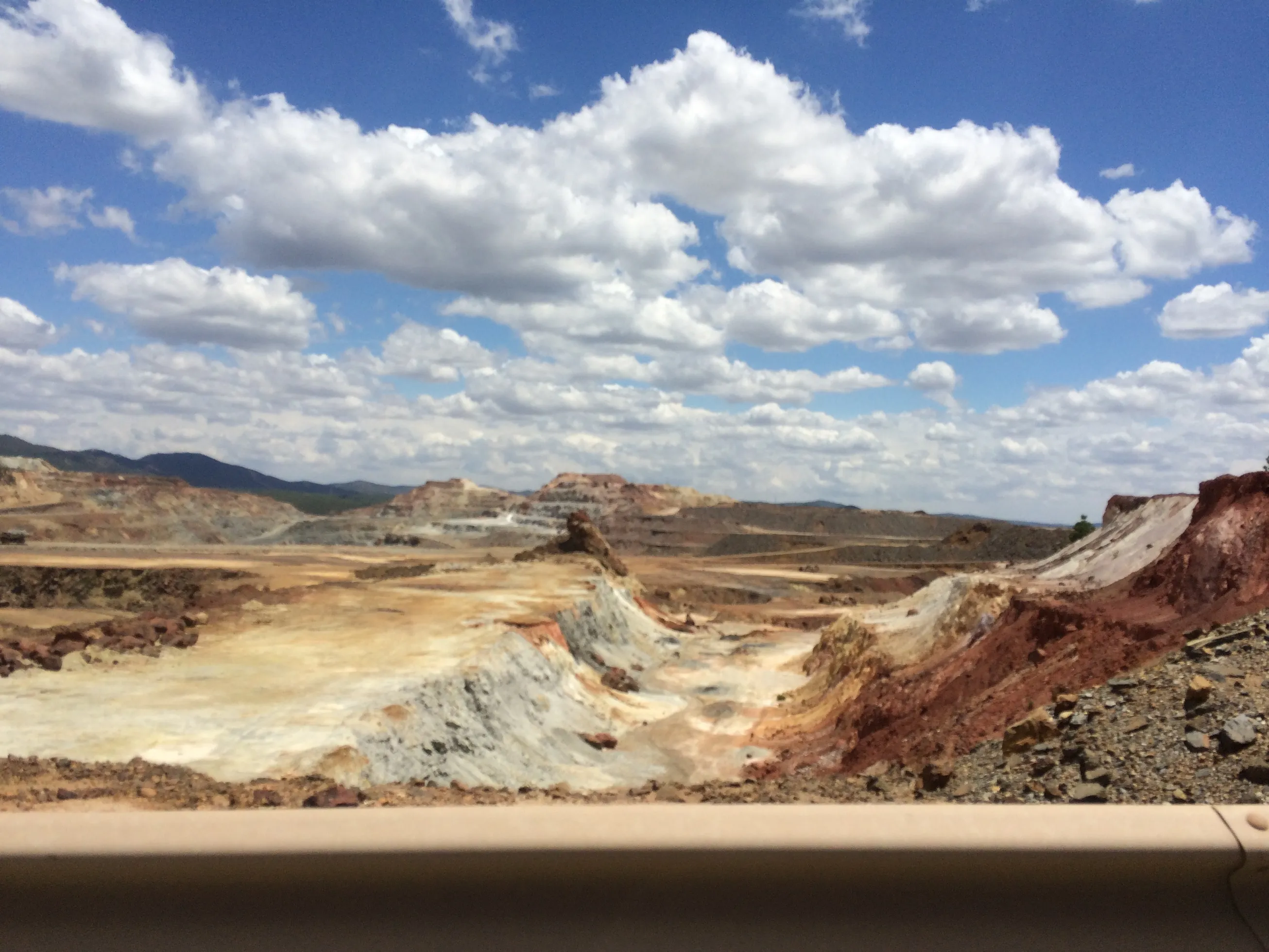 Weathered open-pit mine terrain with red, white and ochre mineral-stained slopes under a cloudy sky
