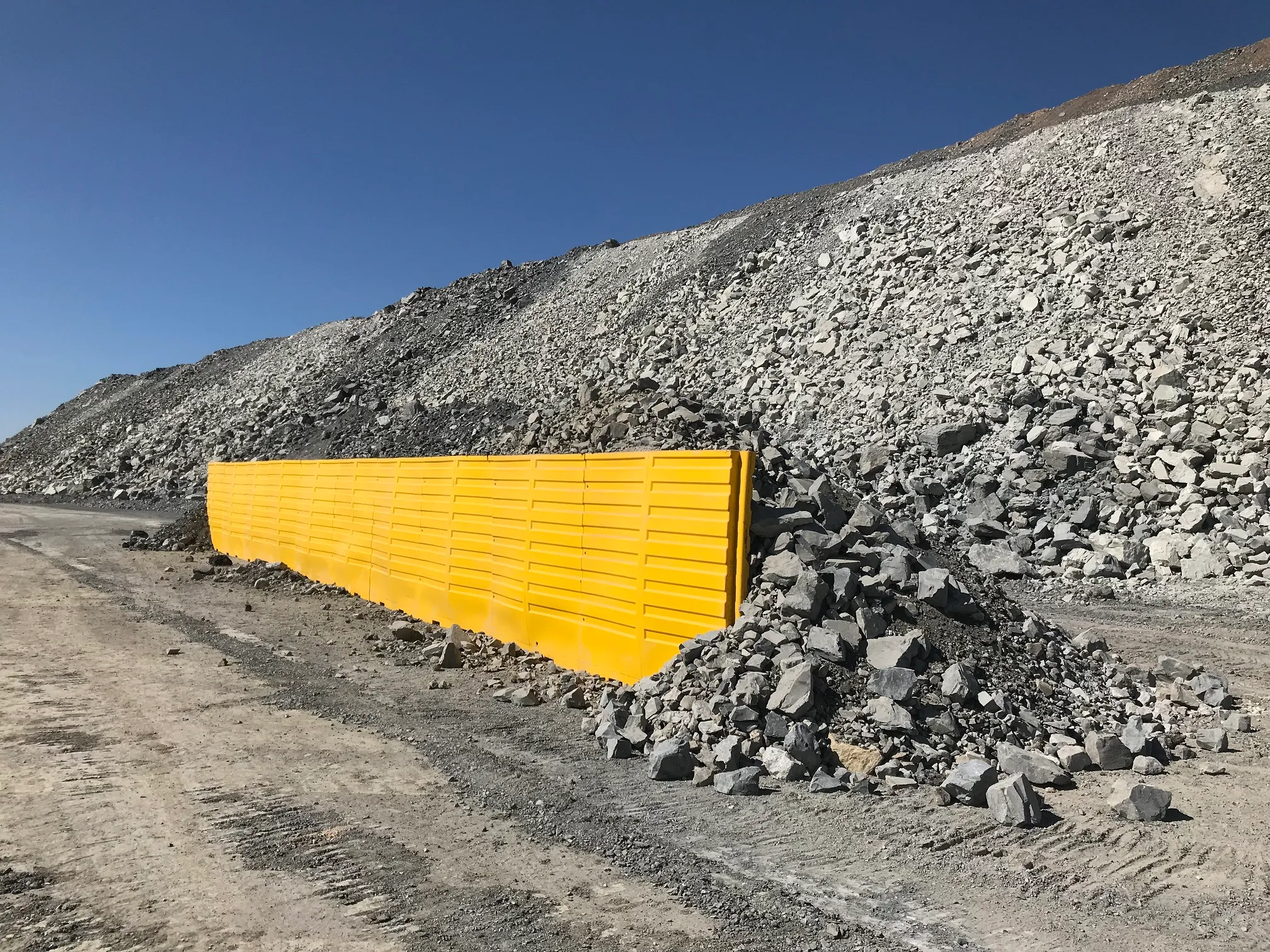 Yellow modular edge protection barrier installed along a haul road at the base of a waste rock dump