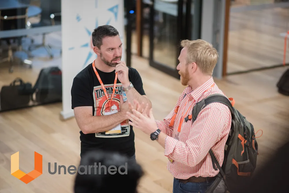 Two attendees wearing conference lanyards discuss ideas during the Unearthed mining hackathon event